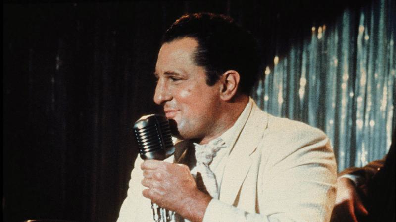 De Niro singing onstage in a white suit jacket, in a scene from Raging Bull