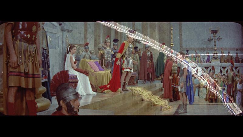 Still of Burton as a Roman emperor in court, with a white streak slanting across the right side of the still