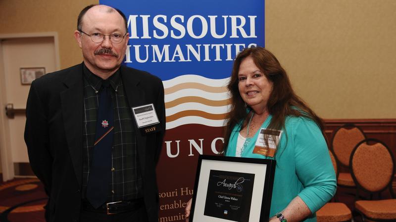 Giglierano and Wallace, posing with Wallace's award in front of a Missouri Humanities poster