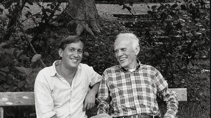 Black and white photo of Walter Isaacson and Walker Percy sitting on a bench, smiling.