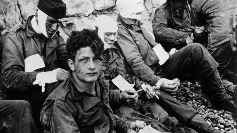Four american soldiers, three with heavy bandaging over their faces, sitting and waiting