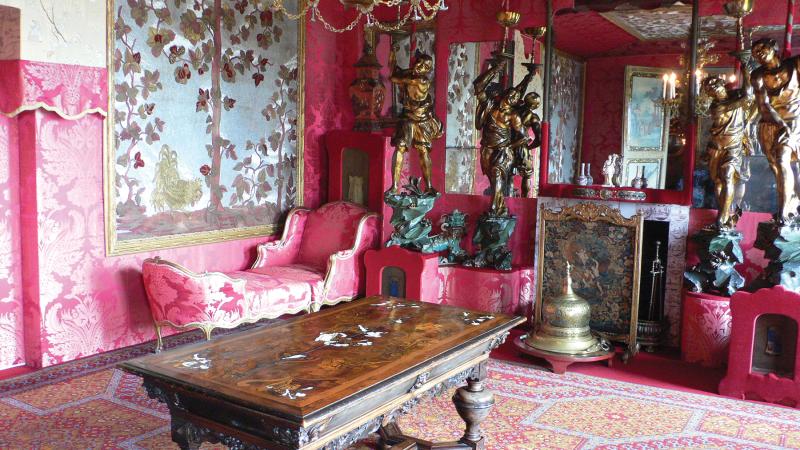 A room in Hauteville House, with bright pink walls, a large wooden table, and ornate, pink furniture