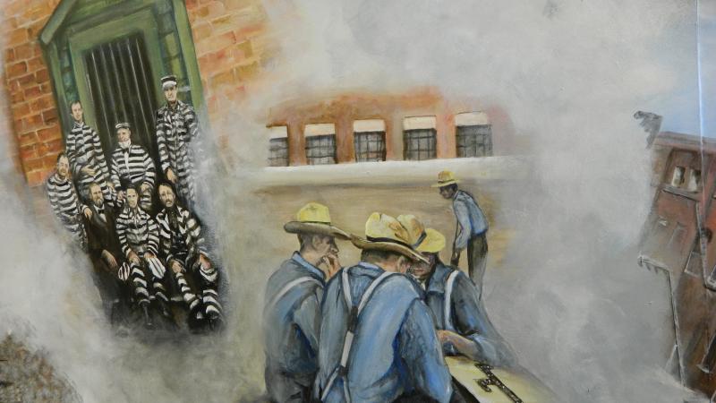 Mural showing prisoners in striped uniforms on the left, and a group of blue shirted men huddled around a table on the right