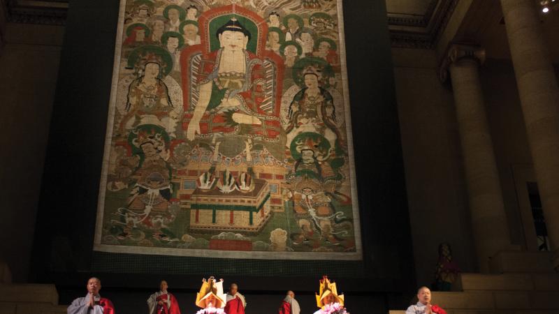The Śākyamuni Assembly, hanging on a stage, with monks performing in front of it