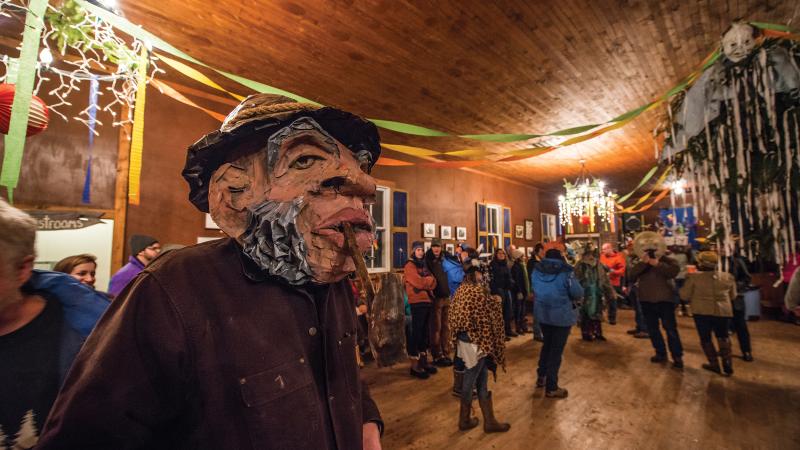 Color photo of a man wearing a mask at a costume festival, indoors.