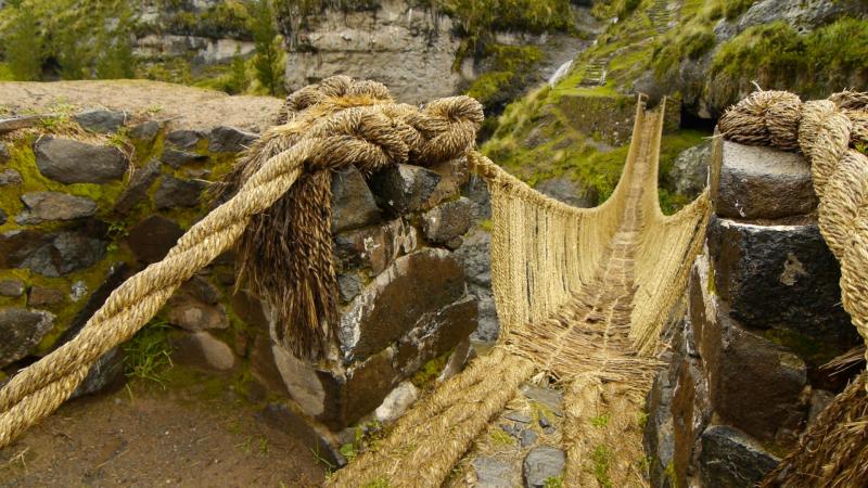 bridge made from thick, braided yellow rope, which dips down and over a chasm, with a river flowing below