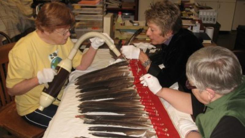 photograph of three women cleaning a feathered headdress