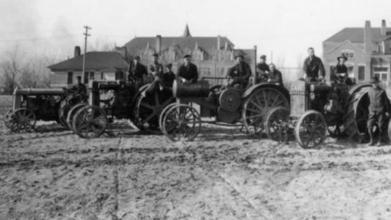 black and white photo of men standing on tractors in field