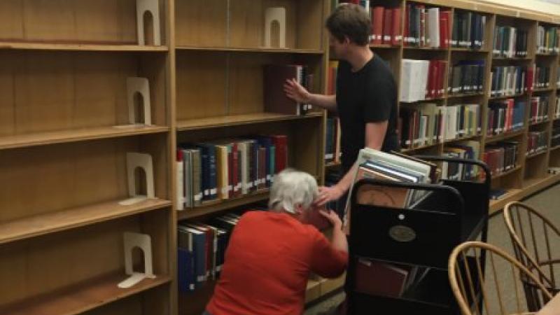 two people removing books from bookshelf