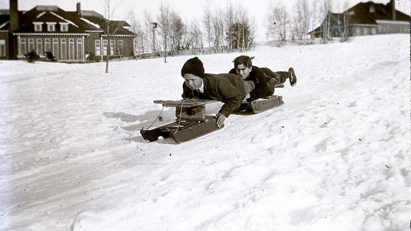black and white photo of two boys sledding down a snowy hill