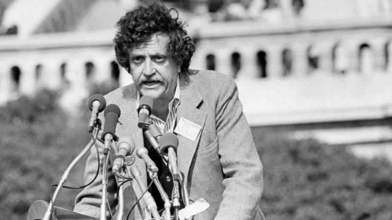 Kurt Vonnegut, speaking publicly, from behind behind a bouquet of microphones