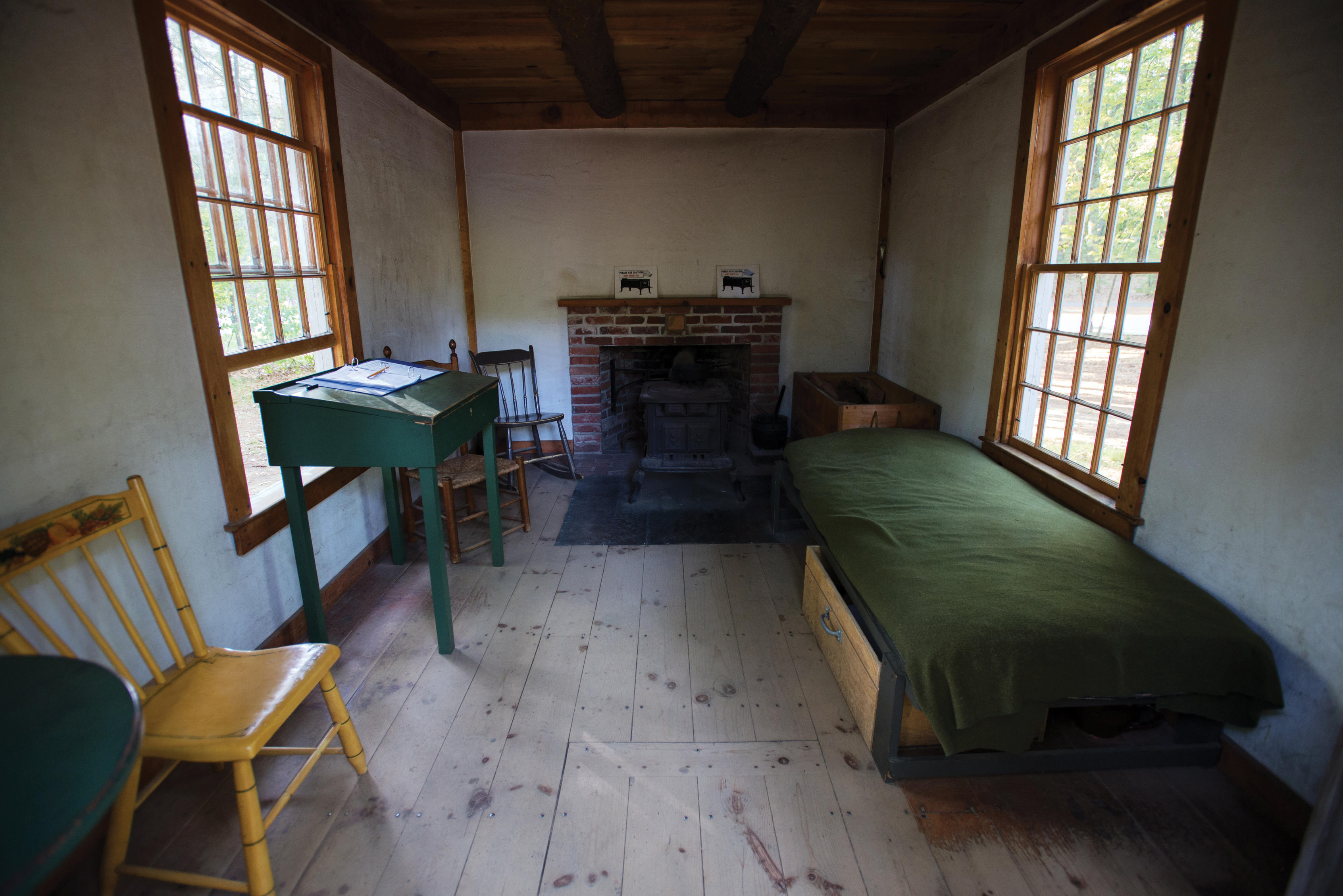 Picture of a basic bedroom with a fireplace, cot, and writing desk.