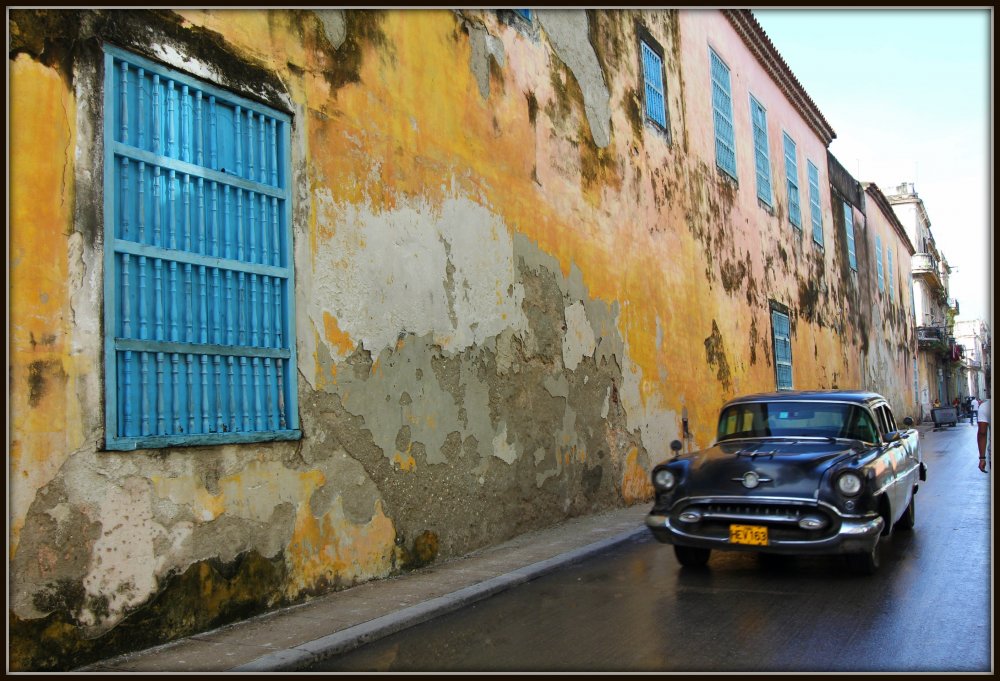Photo of a blue car in front of a yellow wall in havana, cuba