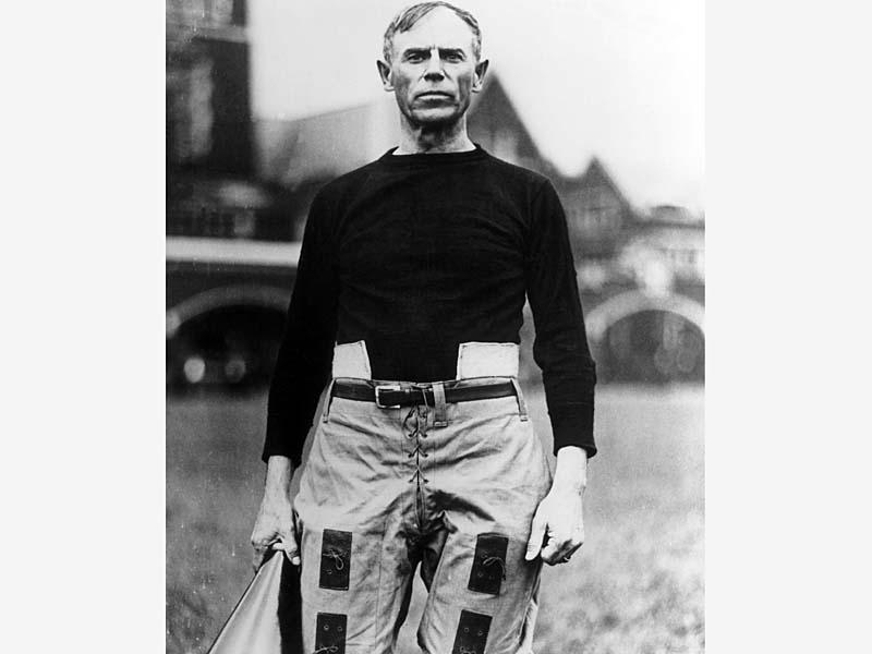 Black and white picture of man standing in black shirt and tan pants