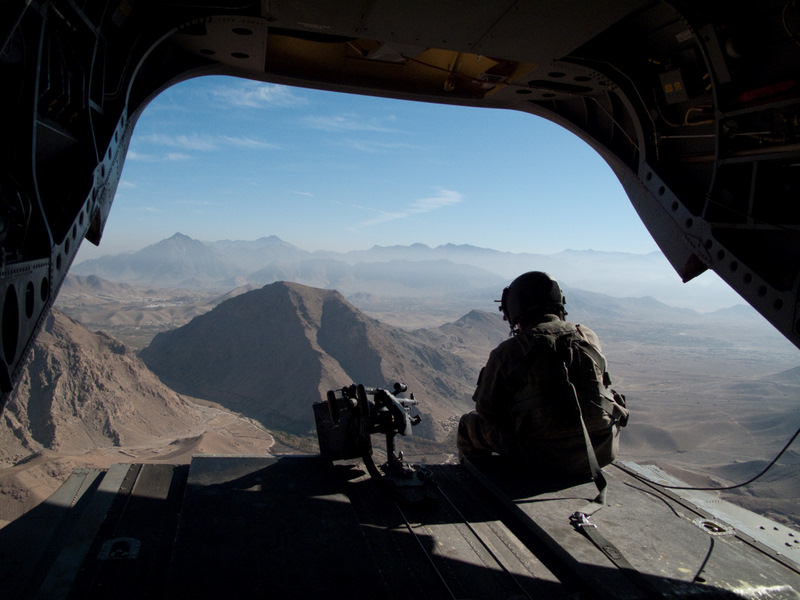 A soldier looking out over mountains in Afghanistan from the back of a cargo plane