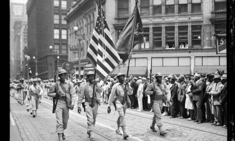 Four color guard from 372nd Infantry marching in front of soldiers	Four color guard from 372nd Infantry marching in front of soldiers