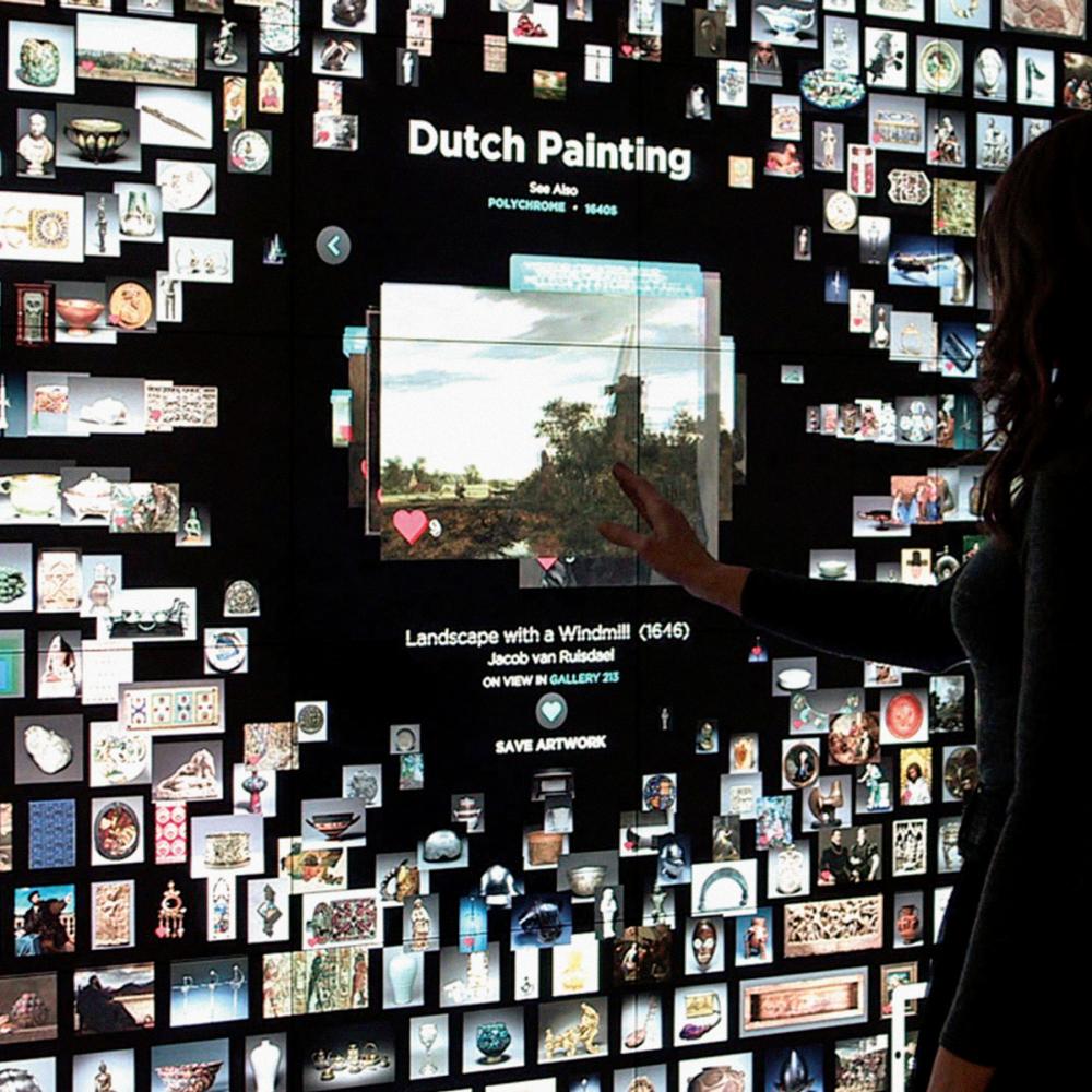 A woman standing before a futuristic touch-screen art catalog at a museum.