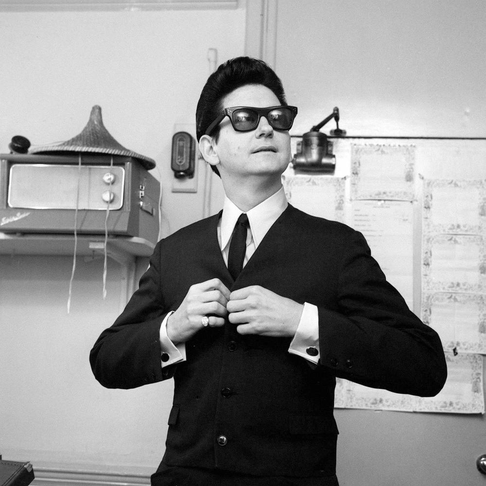 Black and white photo of a man in sunglasses buttoning a jacket