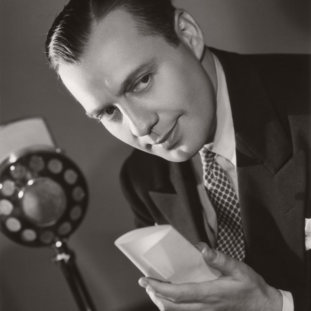 A black and white photo of Jack Benny before a microphone
