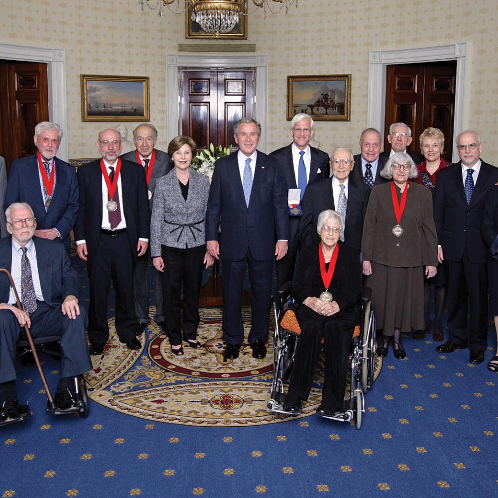 President Bush, standing in the middle of the Medalists wearing their medals, in the Oval Office