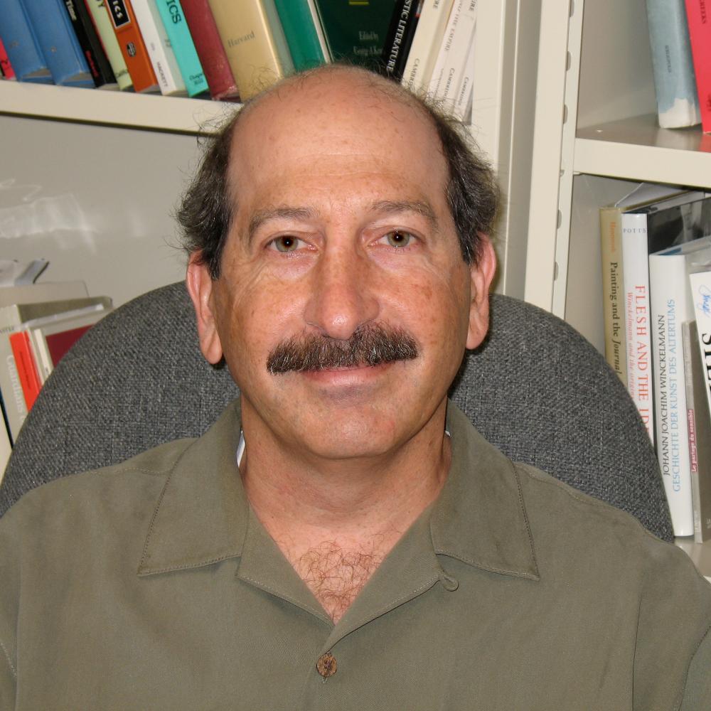Photograph of man sitting in chair, bookshelves behind him