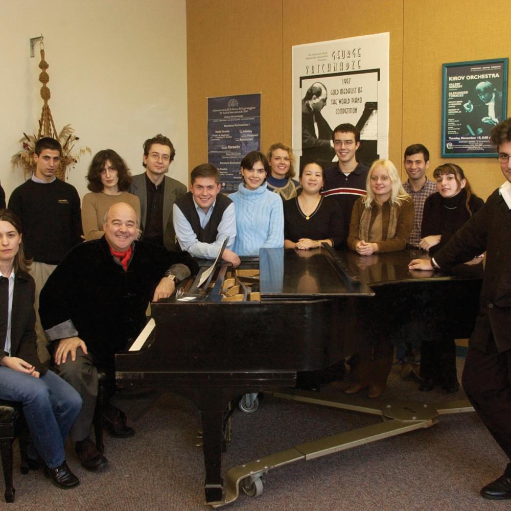 Group photo of musicians standing around a piano
