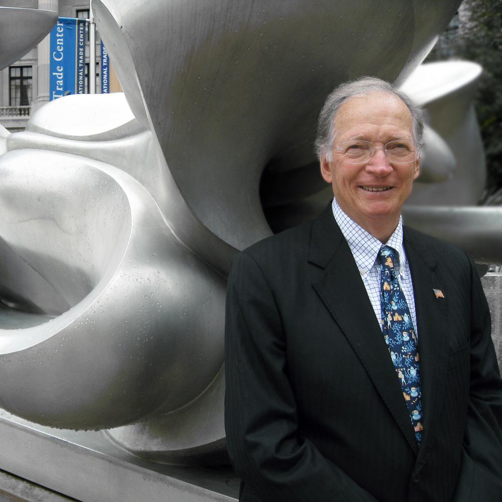 Photograph of man in suit leaning against a contemporary sculputre