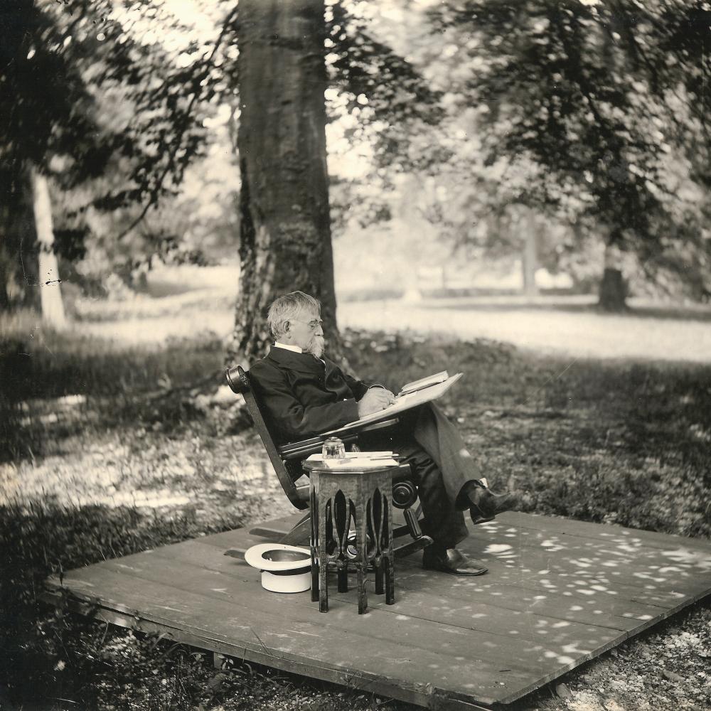 Wallace sits in a rocking chair, writing in pen on a notebook, legs crossed