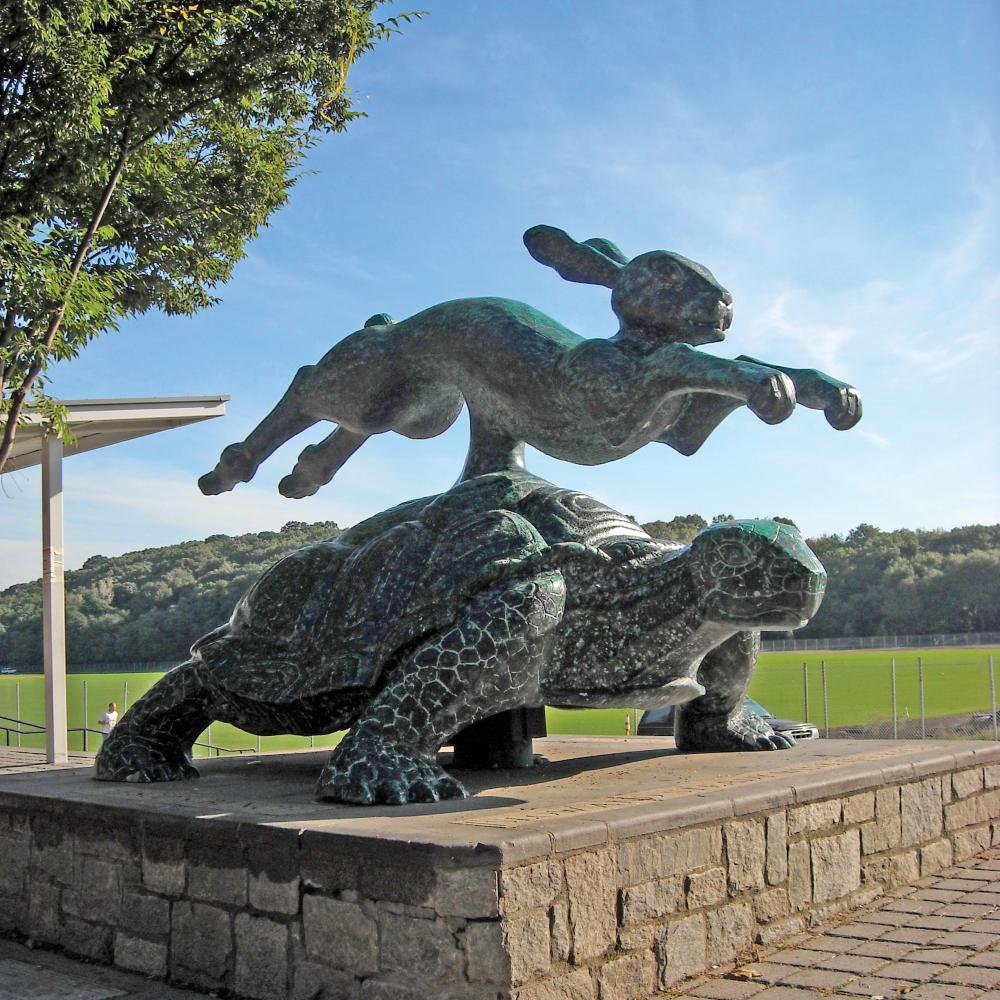 A brass hare leaps over a tortoise in a larger than life sculpture