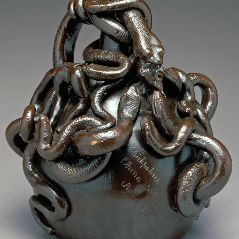 A twining mass of snakes twists around the top of a round jug with a narrow neck