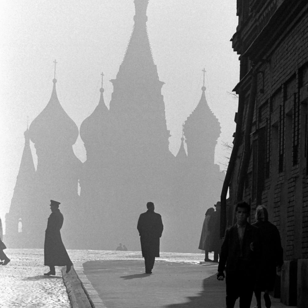 A few people walk on a wide sidewalk, with the shadow of the kremlin rising through the mist in the background
