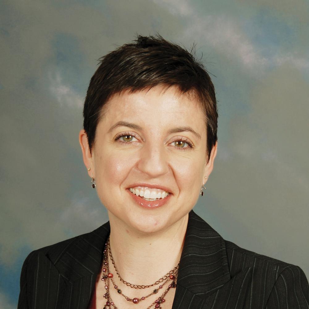 Fitzpatrick smiling, short dark hair, wearing a black blazer, maroon blouse and layered necklace with small maroon stones