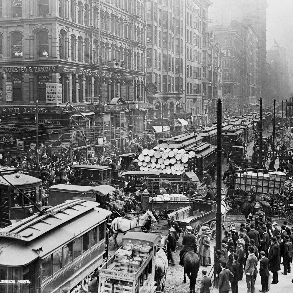 Streetcars, trucks and cars fight to cross an intersection, while crowds of pedestrians move around the gridlock