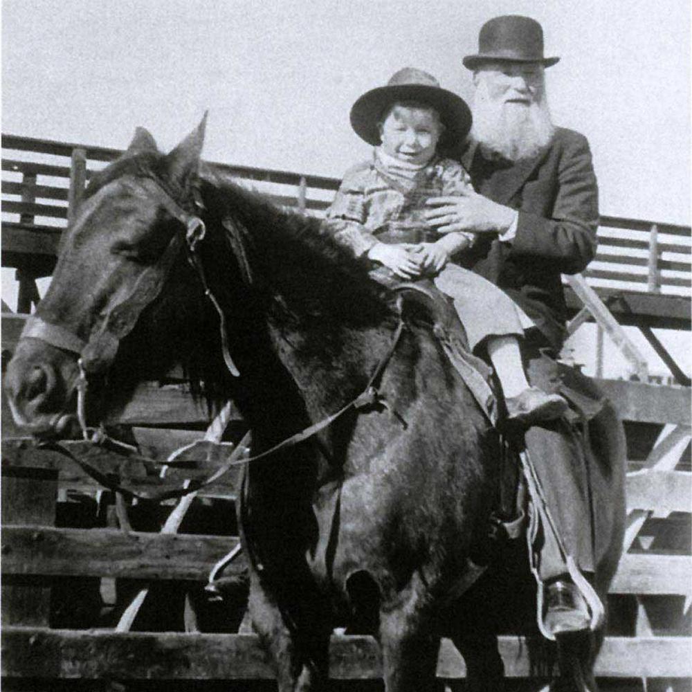 Miller, bearded and wearing a bowler hat, sits behind a young boy on a horse