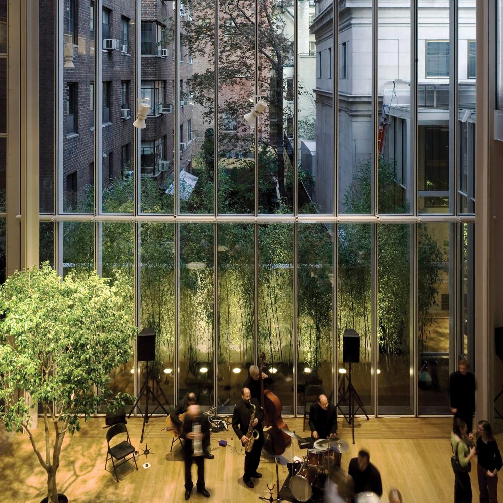 Floor to ceiling windows looking out onto a small green space bordered by tall buildings, a classical quartet plays on a stage in front of the windows