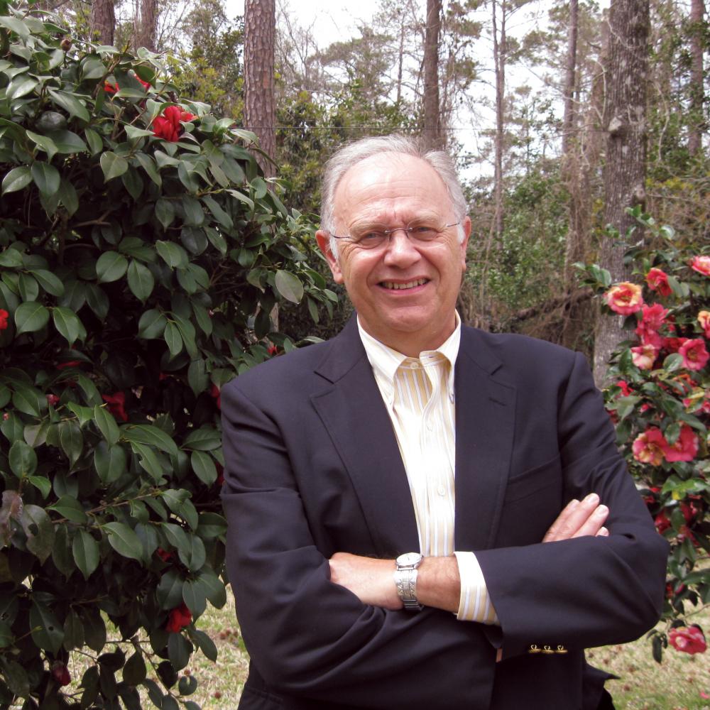 Photograph of a man in a suit standing in rose garden