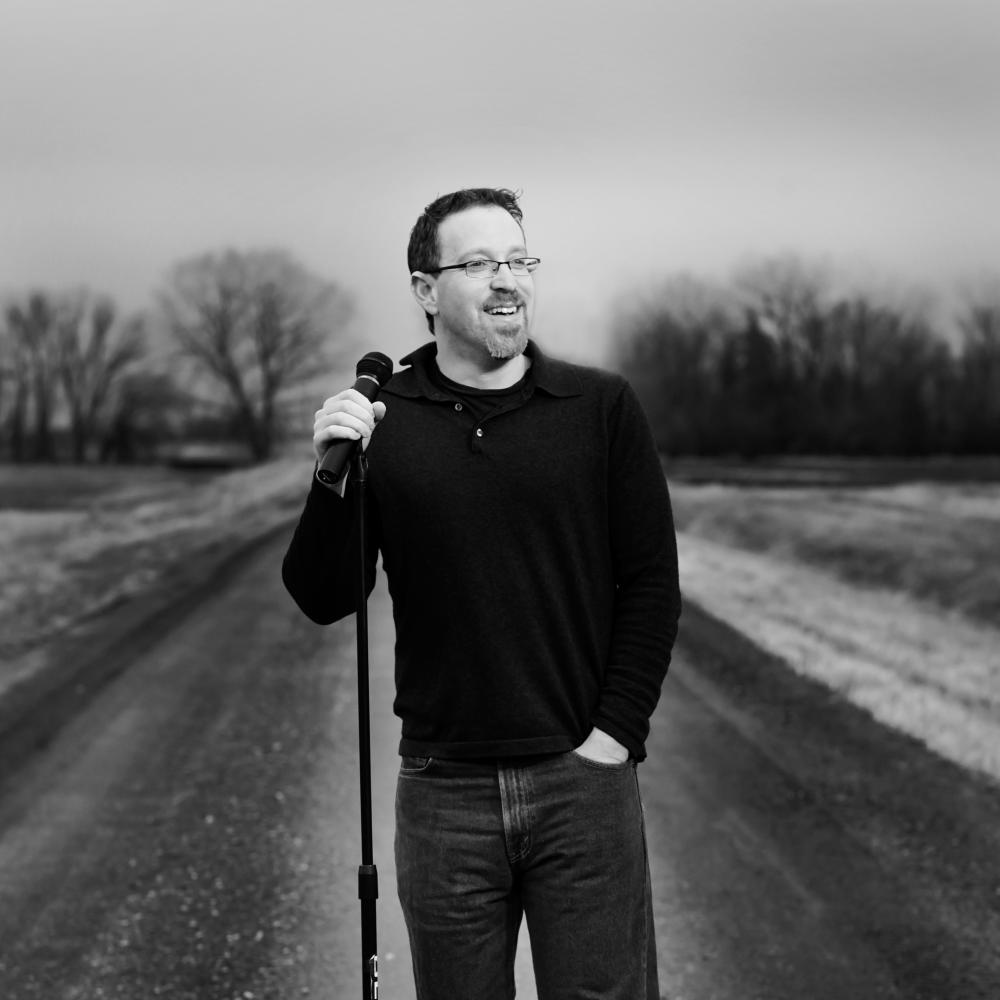 black and white photograph of a man standing in the road, holding a microphone