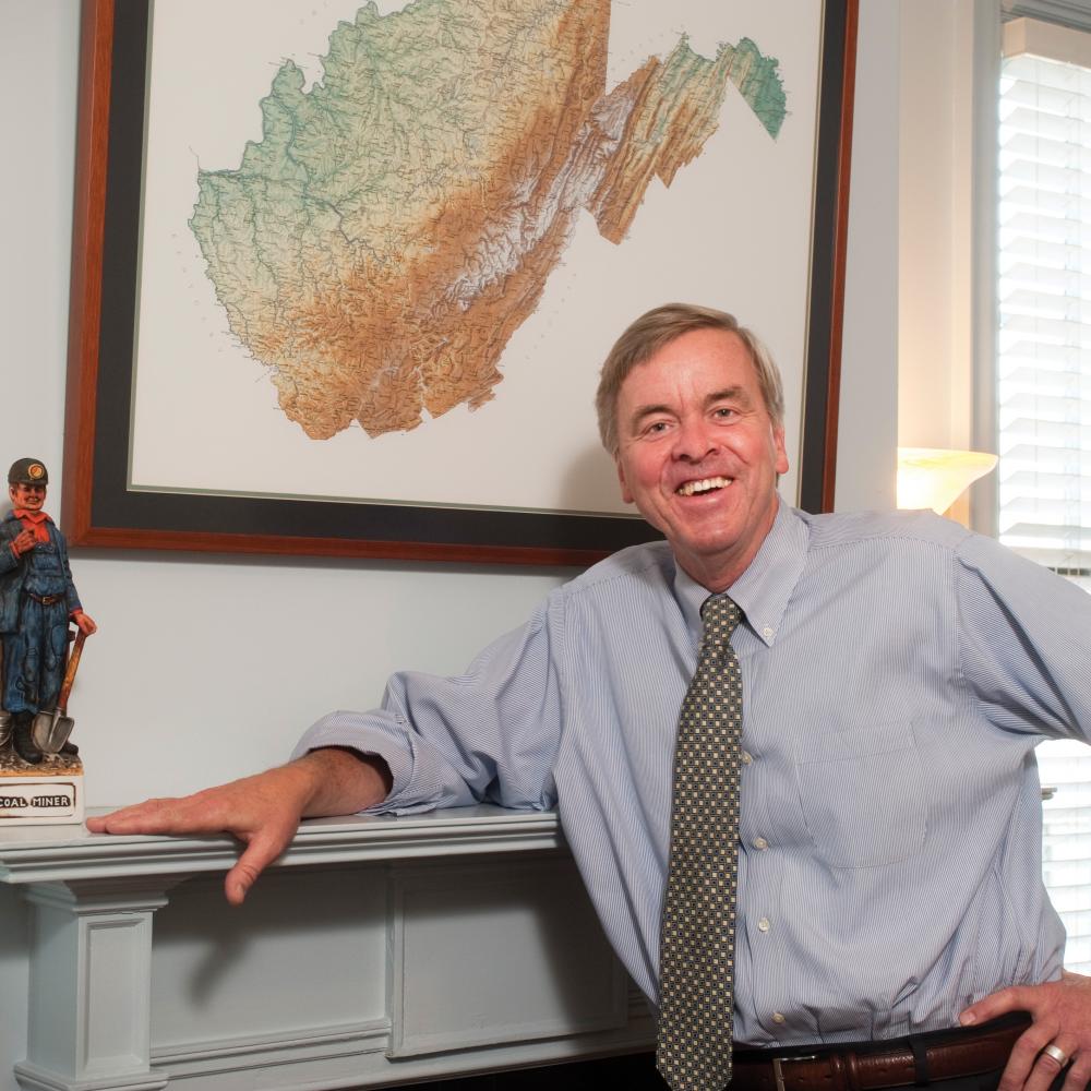 Color photo of Ken Sullivan posing for a portrait next to a fireplace hearth.