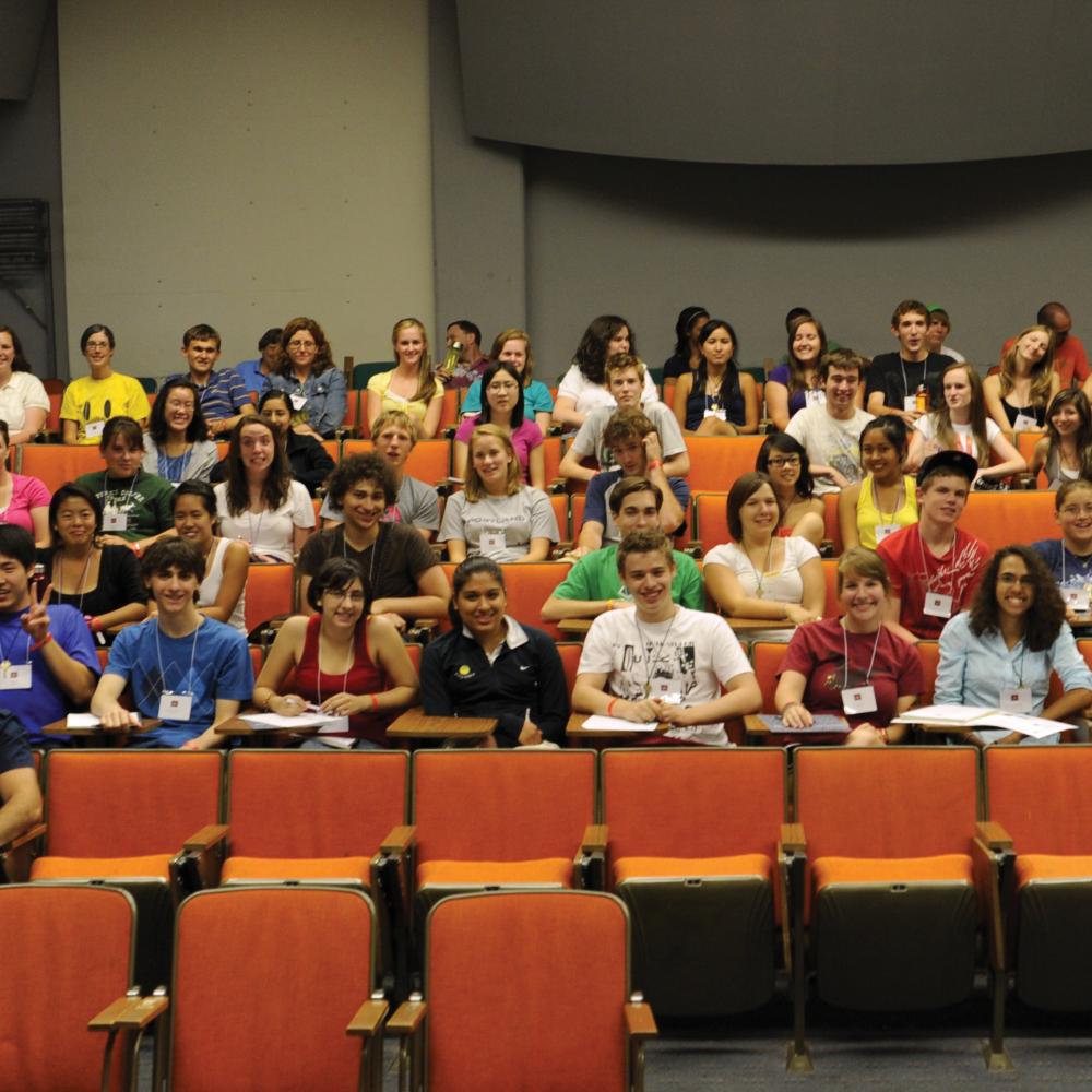 Color photo of many students sitting in an auditorium, smiling.