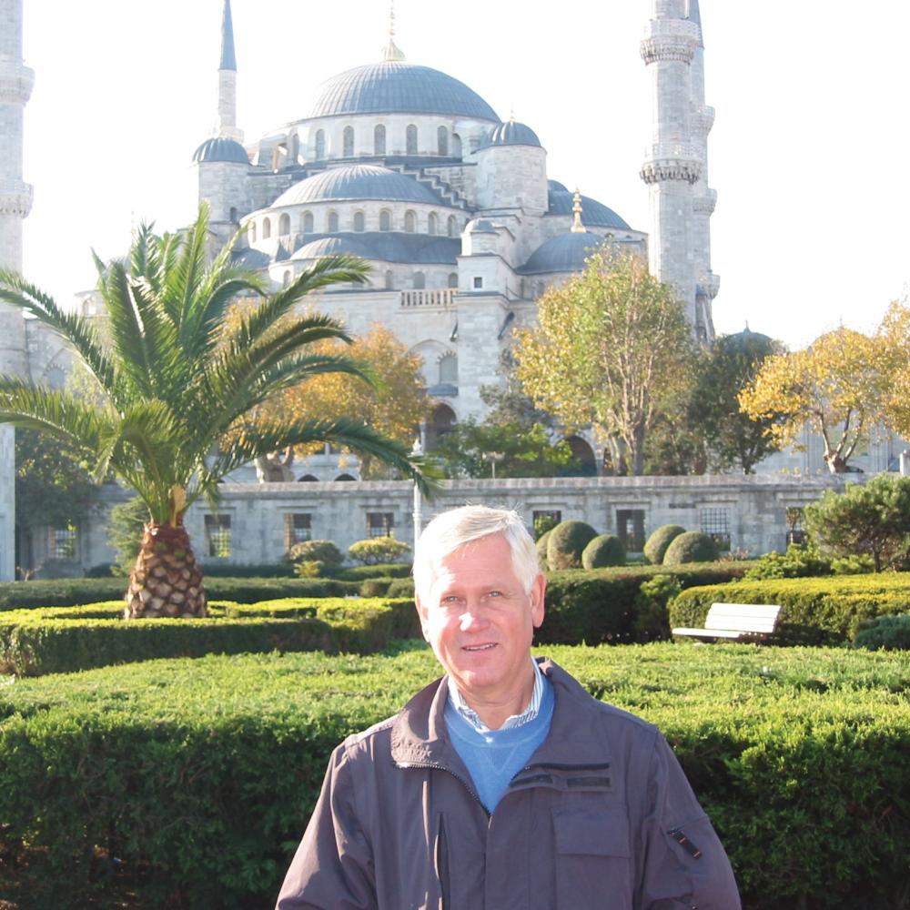 Color photo of Gale Peterson standing before a large mosque and its elaborate gardens.