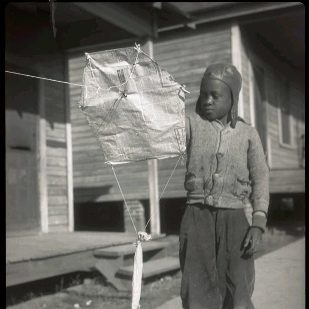 Black and white photo of an African American child playing with a kite.