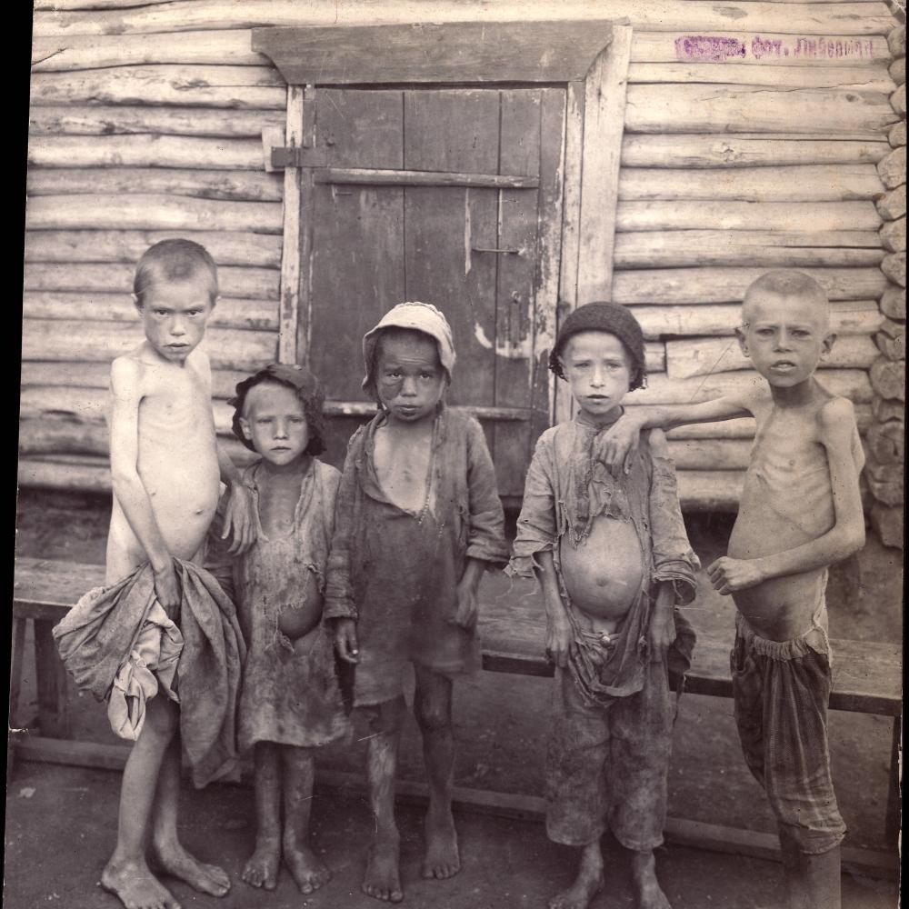 Five children, dressed in rags, stand in front of a wood doorway, stomachs bloated and ribs exposed