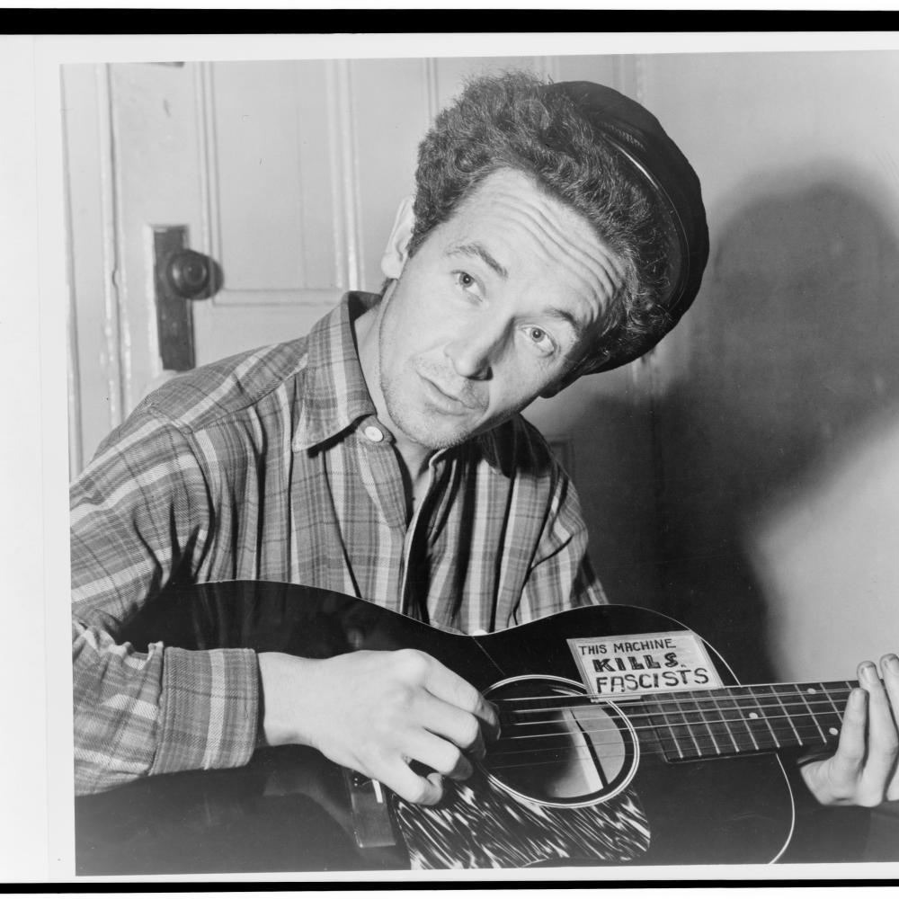Guthrie in a plaid shirt, playing the guitar