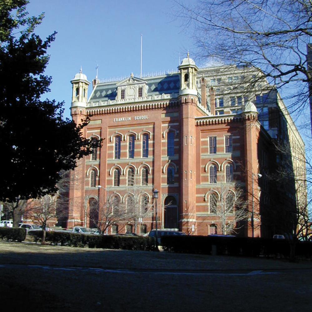 Red brick, five story building with a green tiled roof