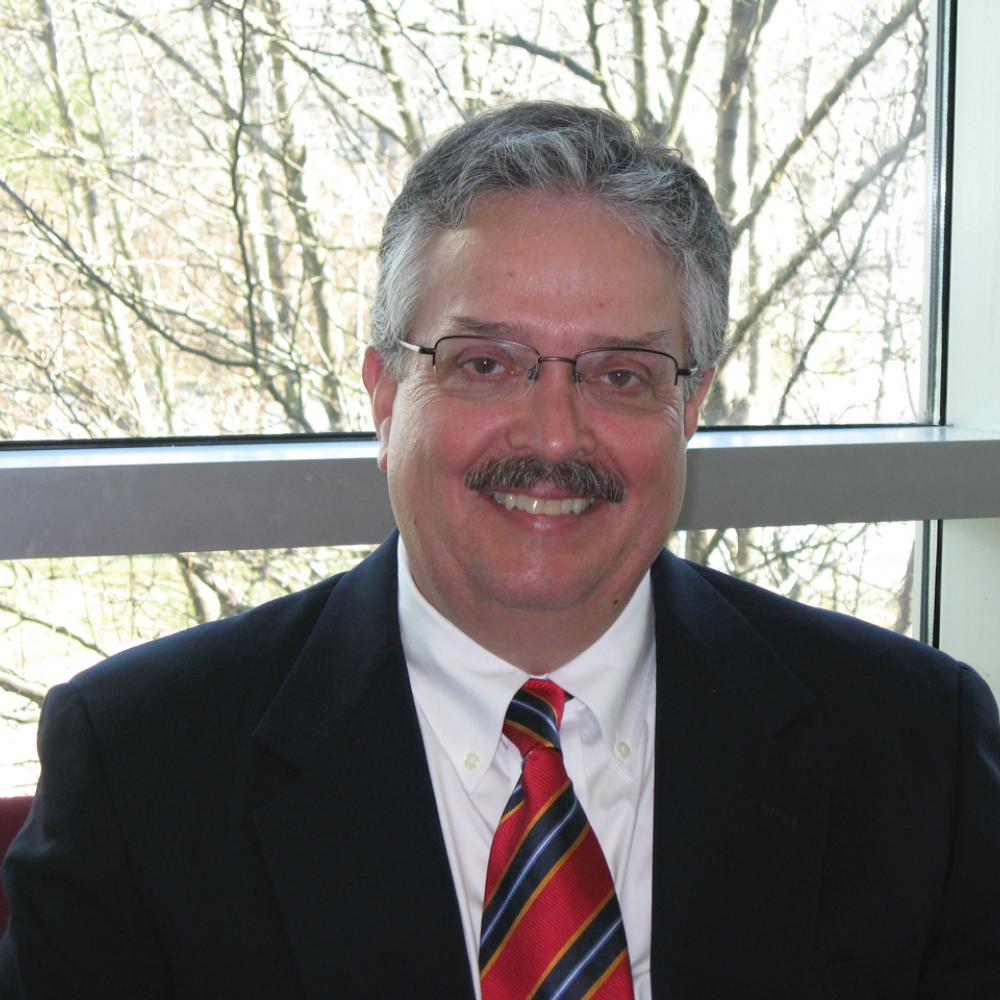 Paul Austin wearing glasses, wearing a red and blue striped tie and dark suit jacket