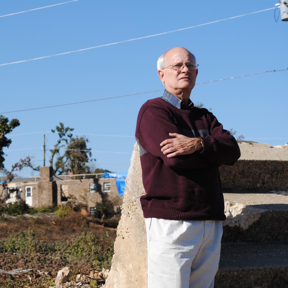 Color photo of Bob Stewart standing amid damaged houses.
