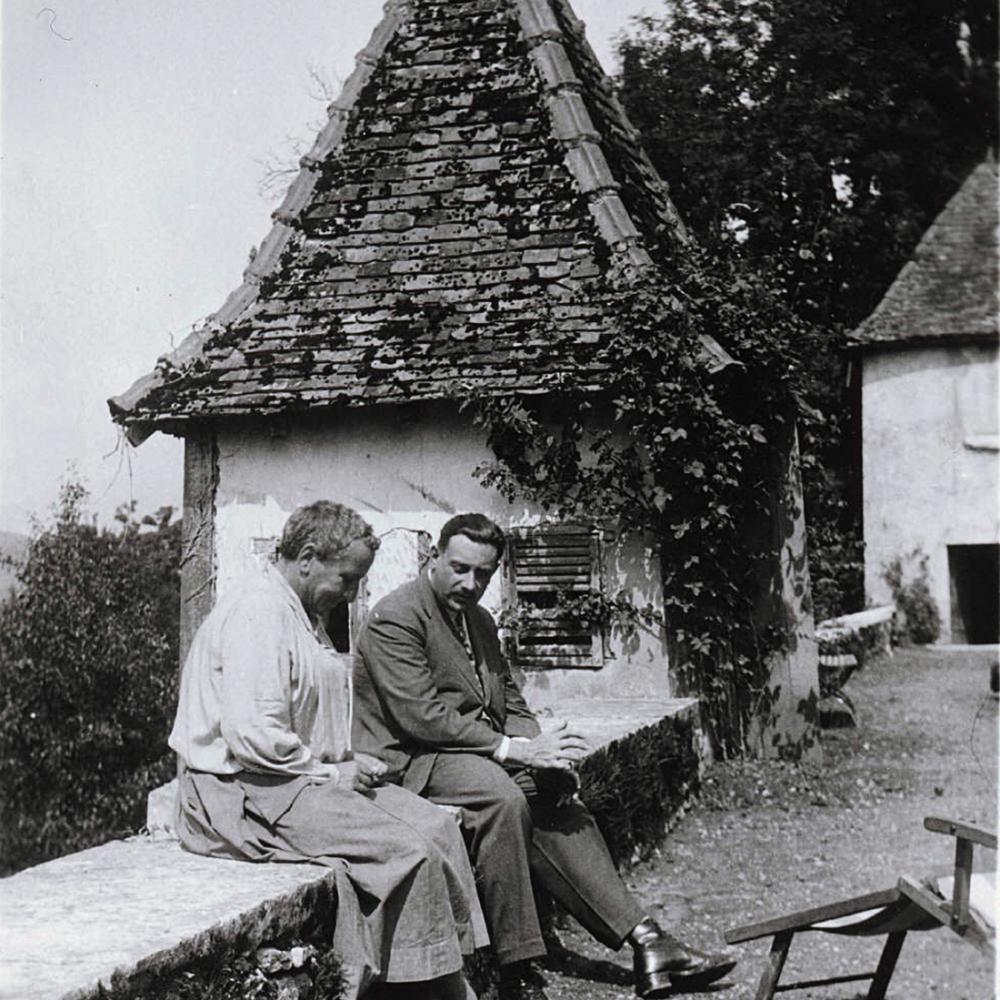 Black and white photo of Gertrude Stein sitting with a male friend on an overlook next to a road.