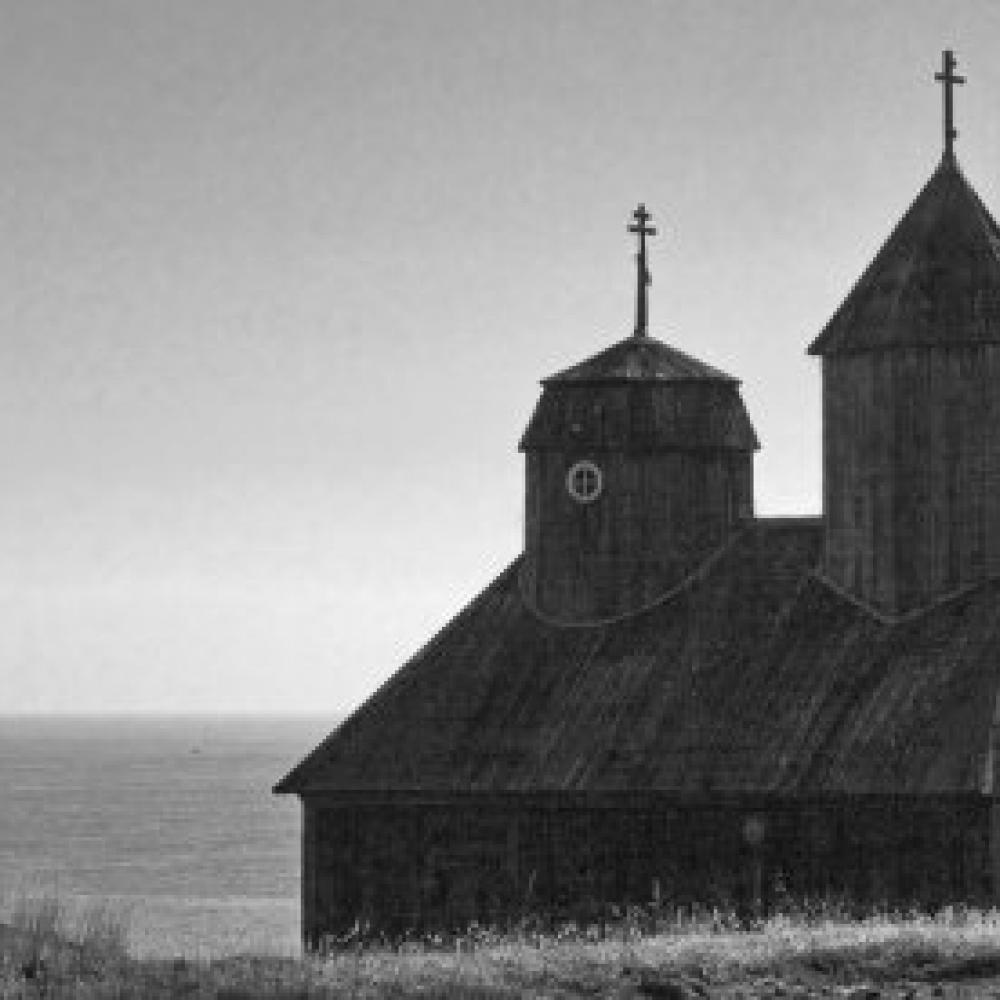 Black and white photo portrait of a seaside church with two cupolas. 