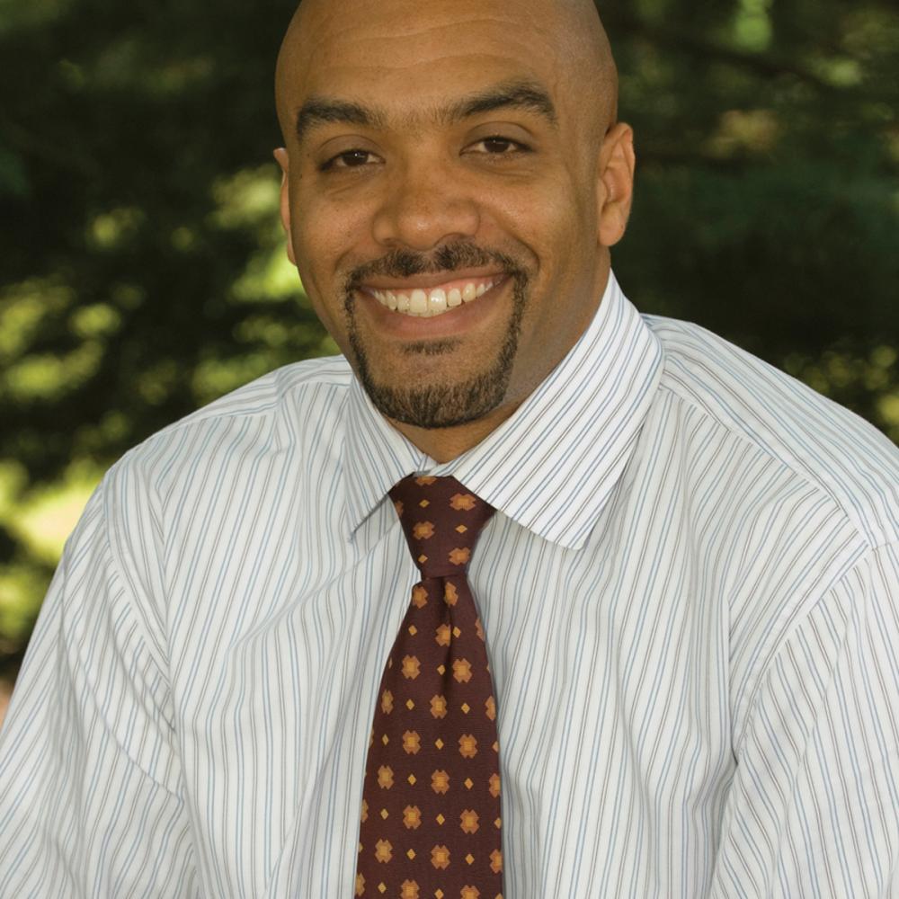 Color photo portrait of Chad L. Williams in a white shirt and burgundy tie.