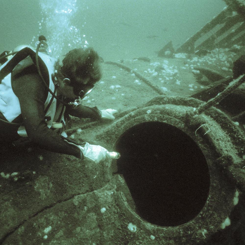 Photo of a scuba diver pointing at the torpedo loading hatch of a sunken submarine.